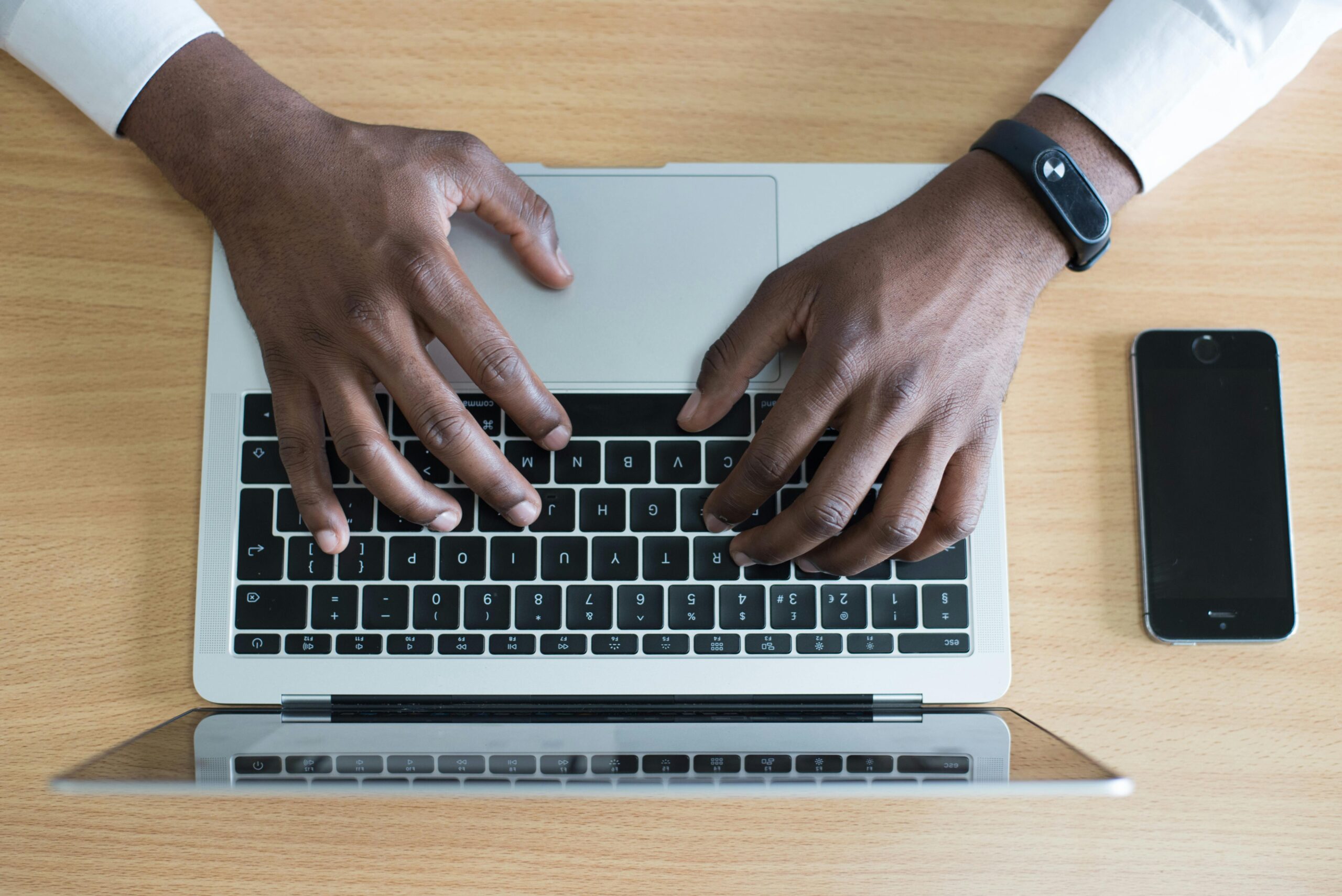 Person typing on a laptop with a smartphone nearby, showcasing modern technology use.